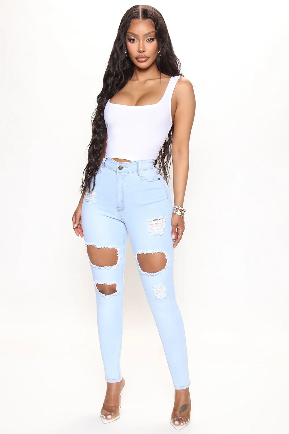 Woman wearing light blue ripped jeans and a white top on a white background