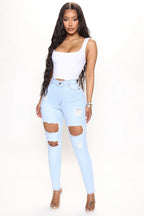 Woman wearing light blue ripped jeans and a white top on a white background